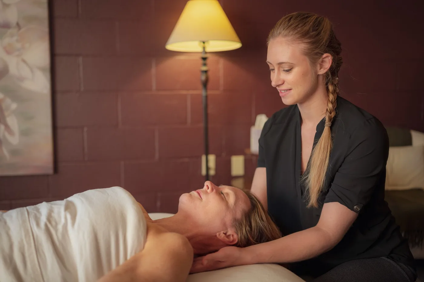 Katie supporting a client’s head and neck at the top of the table in a warmly lit room.