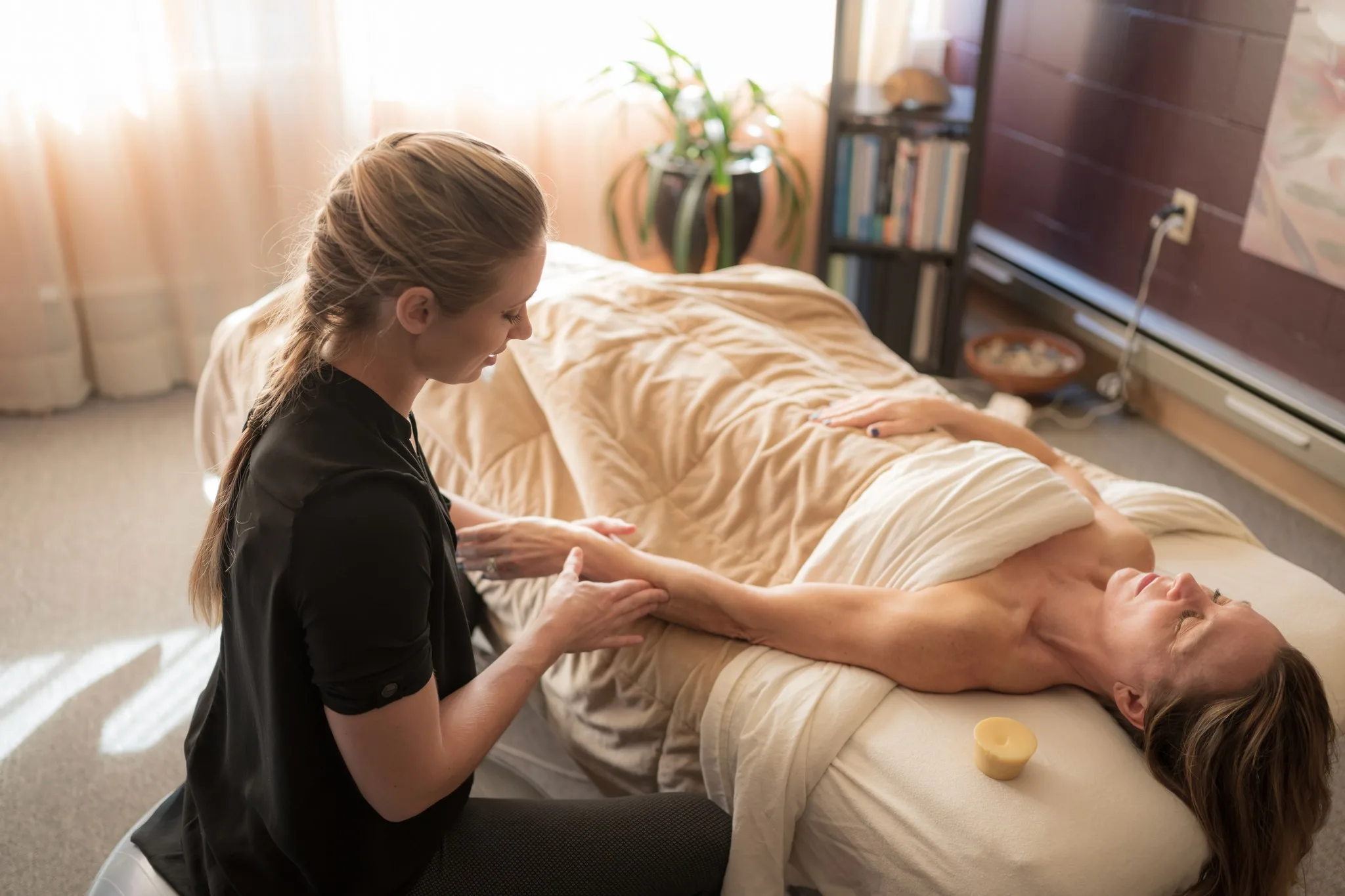 Katie working along a client’s arm and shoulder in a bright treatment room.