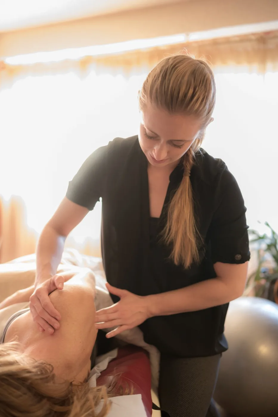 Katie working across a client’s shoulder and neck while they lie face up.